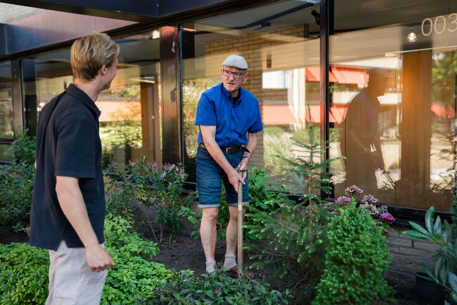 Een jonge gezelschap aanbieder helpt een senior man in de tuin bij zijn woning