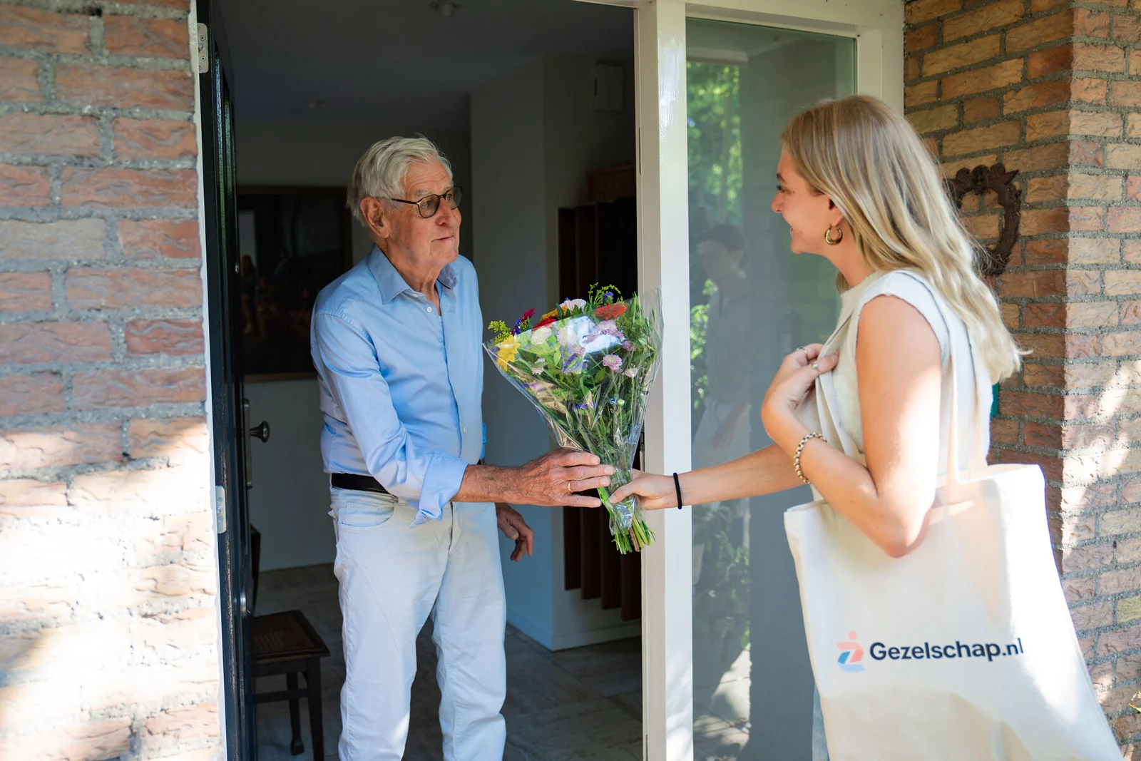 Een gezelschap aanbieder komt met bloemen aan de deur bij een senior man